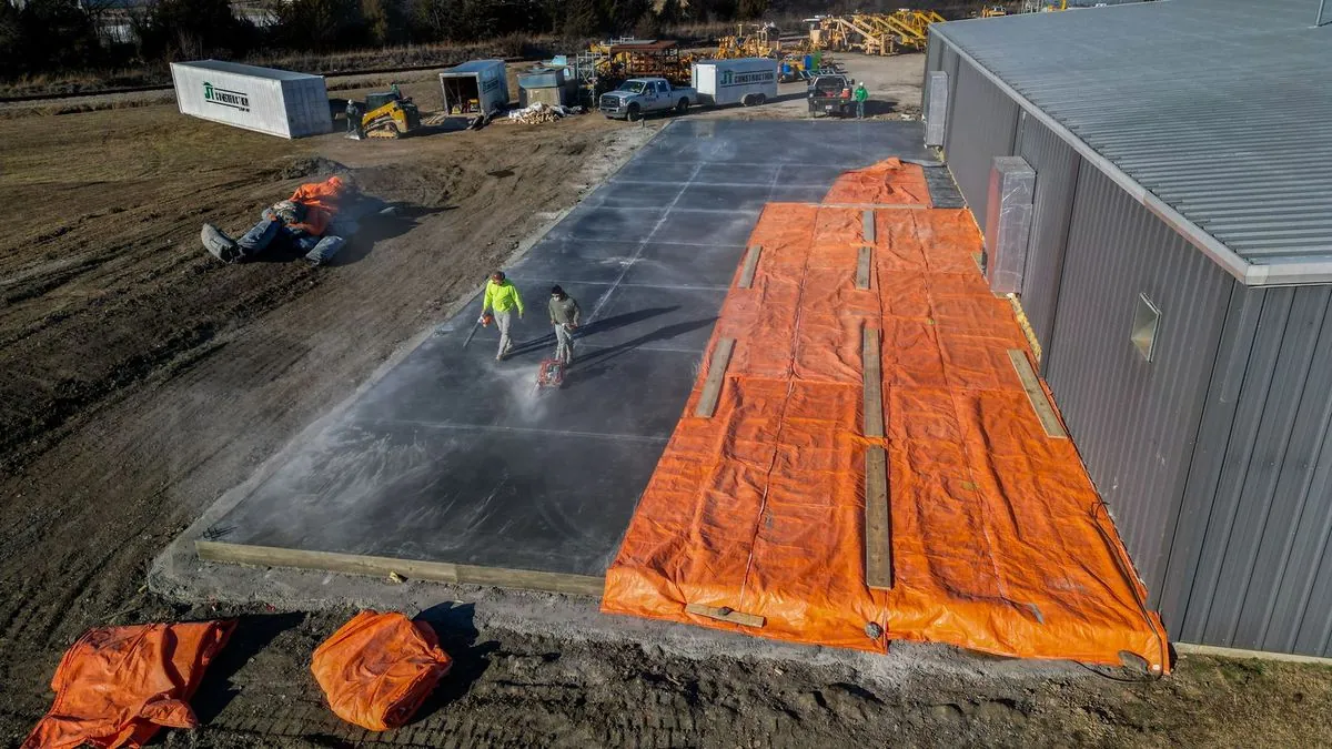 Aerial view of crew finishing concrete slab with orange curing tarps